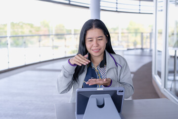 Focused Asian woman engaged in video call or presentation on her tablet, using hand gestures to communicate effectively in modern. Perfect for themes of remote communication, online meetings