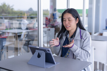 Focused Asian woman engaged in video call or presentation on her tablet, using hand gestures to communicate effectively in modern. Perfect for themes of remote communication, online meetings