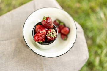 Cozy summer still life: strawberries in a white enamel mug placed on a textured towel on a wooden...
