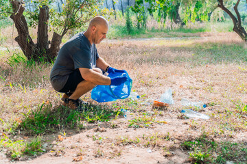 Man as a volunteer picking up trash in forest wearing gloves and using garbage bag