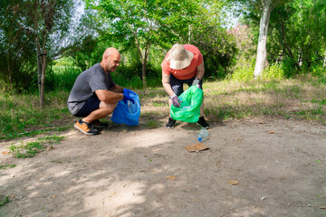 One man and a senior woman as a volunteers cleaning up a forest, collecting plastic bottles and other garbage in bags.