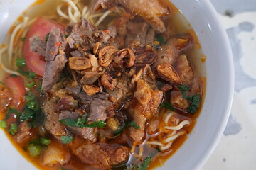 Traditional Indonesian Soto Mie from Bogor, served hot in a white bowl with savory beef, fried shallots, tomato slices, noodles, and fresh herbs.