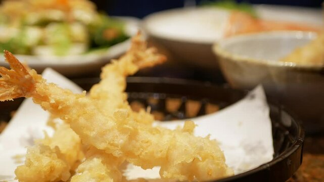 close up selective focus to a plate of crispy prawns temupra japanese food while hand using chopstick to pick up tempura from a plate in lunch dinning restaurant time.deep fried prawns japanese food