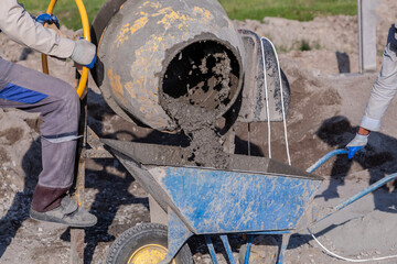 A worker pours cement mortar, concrete, from a concrete mixer into a wheelbarrow. Preparation of...