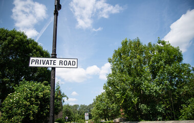 Private road sign with white text on black background, set against a backdrop of lush green trees...