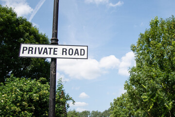 Private road sign with white text on black background, set against a backdrop of lush green trees...