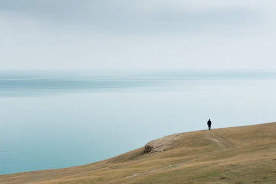 minimalist scene featuring solitary figure standing on coastal cliff in kazakhstan under overcast sky
