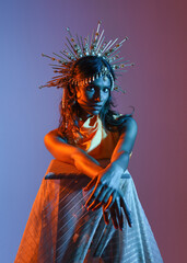  portrait of a female model wearing a  fantasy crown, yellow gown and flowing fabric cape.  Walking pose on studio background with warm golden sunset  lighting