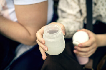 Young mother cooling baby bottle with hot water from a thermos in a park, preparing infant formula safely outdoors