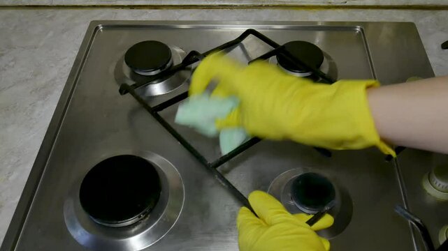 Hands in yellow household gloves wash the grate of the hob