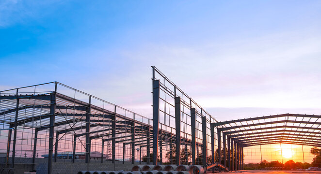 Silhouette steel structure of modern industrial factory building in construction site against sunset sky background, low angle view - Powered by Adobe