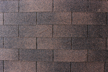 A close up, top down view of asphalt shingles, showcasing their granular texture and varying shades of dark brown and black.