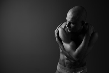 Obraz premium A contemplative man poses gracefully in a black and white setting, showcasing strong muscles and a reflective mood with an artistic touch.