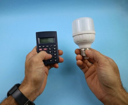 Hand Holding LED Bulb and Calculator with Blue Background. energy saving concept. top view