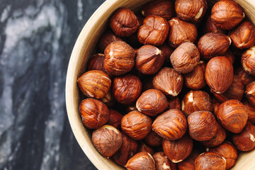 Hazelnuts in ceramic bowl on dark marble background. Crunchy brown snack food. Natural dry ingredient. Closeup macro texture. Rustic kitchen healthy composition. Organic vegetarian diet source.