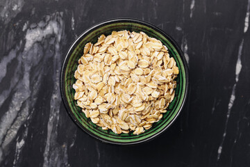 Rolled oats in green ceramic bowl. Dry oat flakes on dark marble background. Healthy breakfast...