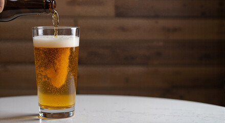 Glass of beer being poured from brown bottle on wooden table background