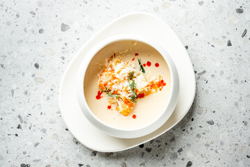 Gourmet creamy soup with shredded crab meat, fresh dill, and red sauce drops, elegantly served in a white bowl on a stone-textured background.
