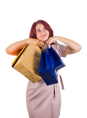 Young redhead woman with hands under chin carrying multiple shopping bags looks up dreaming isolated on transparent background
