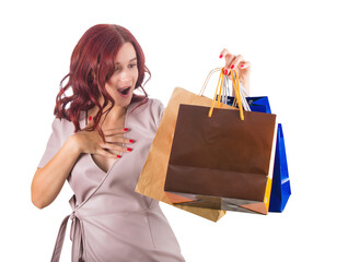Surprised redhead woman keeps hand to chest while holding multiple shopping bags in her hand