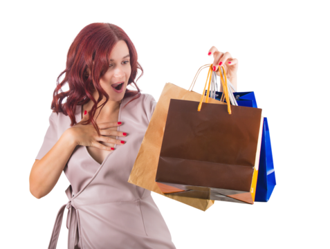 Surprised redhead woman keeps hand to chest while holding multiple shopping bags in her hand