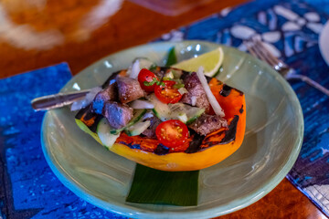 Grilled papaya salad with beef, tomatoes, cucumbers, and lime on a green plate.
