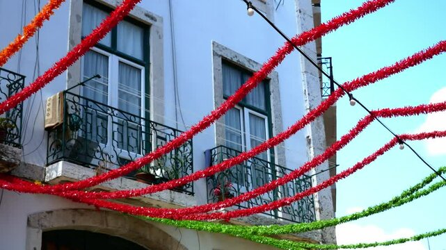 Colorful red, orange, and green garlands stretch across the street in front of a traditional Lisbon building, decorated during local folk celebrations of Feast of Saint Anthony. Portugal.