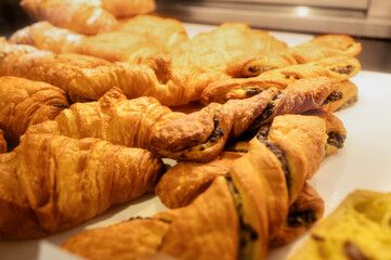 Close-up of freshly baked croissants and chocolate twists arranged on a white plate in a warm cafe setting. Pastry ready to serve.