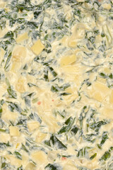 A vertical close-up shot captures the creamy, unbaked filling of a spinach and cheese pie, showing chunks of cheese and green spinach leaves