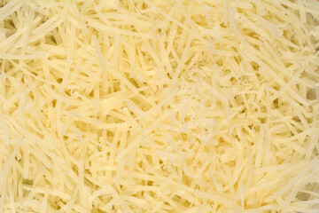 A vibrant, close-up, top-down view showcases a heap of finely grated light yellow cheese, filling the entire frame with its textured strands