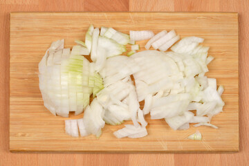 A pile of roughly chopped white onion is spread across a light wooden cutting board, ready for...