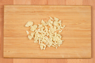 A pile of freshly minced garlic is centrally arranged on a light wooden cutting board, ready for...