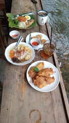 Authentic Indonesian Feast: Nasi Uduk, Fried Chicken, and Snacks Served on a Rustic Wooden Table by a River