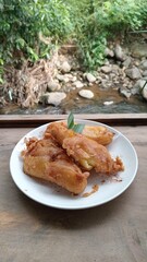 A tempting plate of golden-brown Indonesian fried bananas, a popular local snack, is presented on a wooden surface with a natural green backdrop.