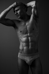 Naklejka premium Athletic man posing in black and white, showcasing his fit physique. The dramatic lighting highlights muscular details and creates a striking silhouette.