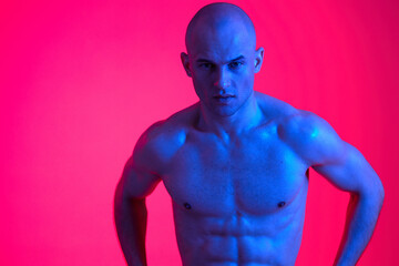 Fototapeta premium Strong man posing in vibrant blue light, showcasing athletic physique. The dramatic colors create an engaging and energetic atmosphere, highlighting his defined muscles.