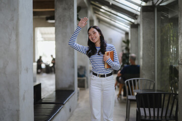 Asian student waving while walking in university corridor