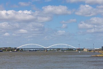 The majestic Merwedebrug Gorinchem (Merwede Bridge) spans a wide river under a bright, cloudy sky, showcasing modern infrastructure and Dutch waterways.