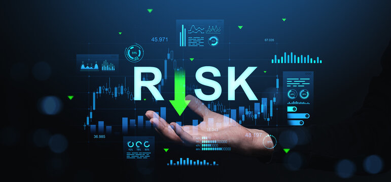 Businessman hand showing word "RISK" with downward arrow and financial data holograms on dark background representing investment risk management concept.