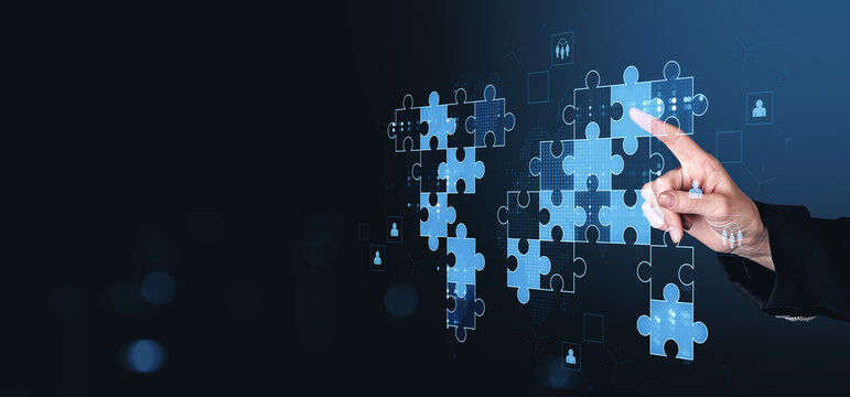 Business hand placing puzzle pieces forming world map representing teamwork, global collaboration, innovation and success on blue digital background.