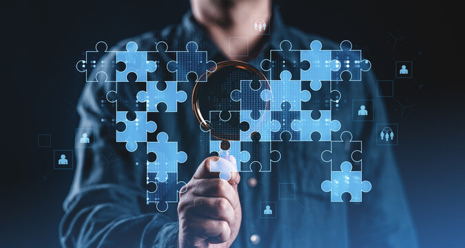 Businessman analyzing digital puzzle pieces with magnifying glass on dark background.