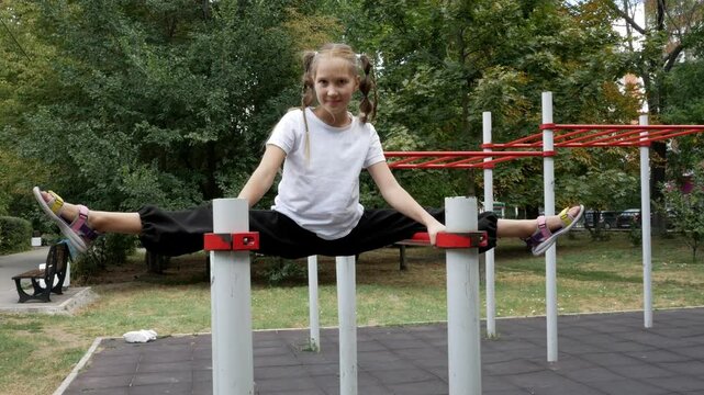 Acrobatic gymnast girl does leg stretching on the outdoors sports ground on top. Acrobatic exercise on the horizontal bar and does sports trick splits at height