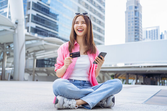 Happy Asian girl sitting on floor using smartphone and holding credit card with enjoys freedom.