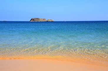 Portugal, Algarve, Sagres, beautiful turquoise Atlantic Ocean with crystal clear water washing onto a deserted Martinhal Beach with powdery sand. Clear horizon. Blue sky.