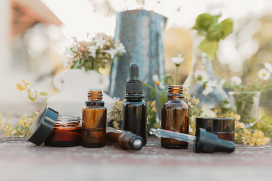 Collection of various amber essential oil bottles with assortment of flowers and herbs in natural ou