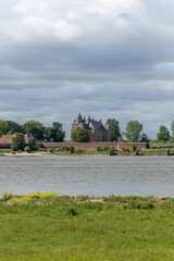 Loevestein Castle, a captivating medieval fortress in the Netherlands, seen across the river under a beautiful, cloudy sky.