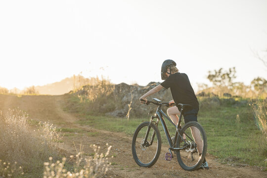 Teenage boy riding mountain bike in rural countryside bathed in golden afternoon light