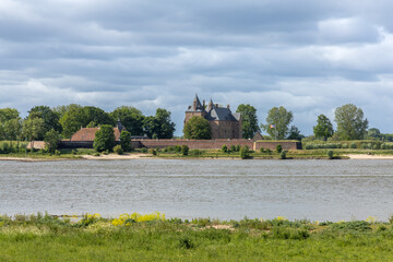 Historic Loevestein Castle, a medieval fortress in the Netherlands, stands majestically across a wide river under a dramatic cloudy sky.
