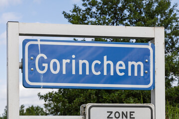 A prominent blue Gorinchem city sign stands against a backdrop of lush green trees and modern Dutch homes, marking the entrance to this historic Netherlands town