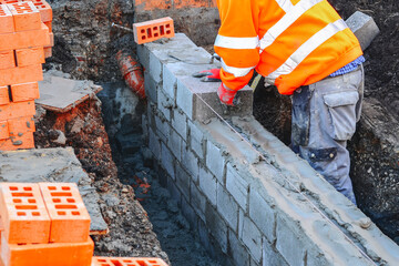 Hard working bricklayer laying concrete blocks on top of concrete foundation ground beam on new residential housing site. Fight housing crisis by building more affordable houses concept